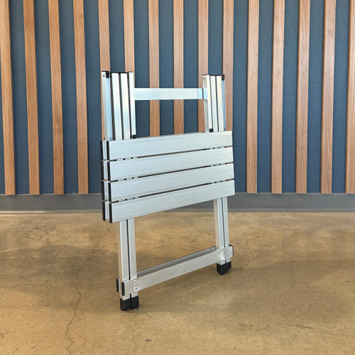 PK Grills Aluminum Compact Foldable Table, a portable aluminum table in folded position with a modern design, lightweight construction, and black feet, suitable for outdoor or camping use.