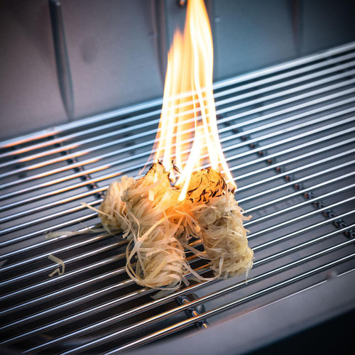 PK Grills PK300 Start Cookin' Bundle - Silver, showing a flaming torch lighting a pile of wood chips on a stainless steel grill grate for outdoor grilling.