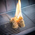 PK Grills PK300 Start Cookin' Bundle - Silver, showing a flaming torch lighting a pile of wood chips on a stainless steel grill grate for outdoor grilling.