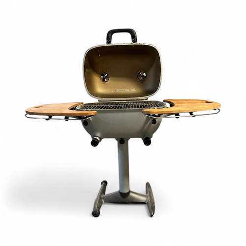 PK Grills PK360 Mismatched with Teak Shelves, imperfect BBQ grill with side shelves made of teak wood, open lid showing grill grate, on a metal stand.