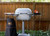 PK Grills PK360 Start Cookin' Bundle - Silver, outdoor kitchen grill with side tray, thermometer, and carrying bag, set against a wooden fence and greenery.