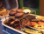 PK Grills The Littlemore Grid for PK Grills, metal grilling rack with burger patties, sausages, and vegetables on a barbecue grill.